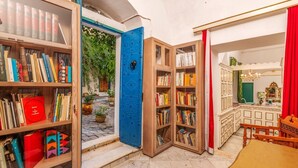 A room with open bookshelves filled with books, a blue door leading outside, and a dining area with a table and chairs. - La Demeure Médina (Tunis)
