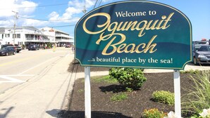 A welcome sign for O'gunquit Beach with a clear view of the surrounding area including a building with a sign that reads "Motor Inn".