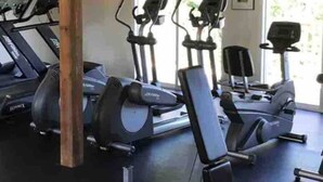 A gym with multiple treadmills and elliptical machines, wooden beams on the ceiling, and large windows allowing natural light.