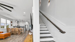 A modern kitchen with white cabinets, a wooden dining table, and a staircase with dark wooden steps.