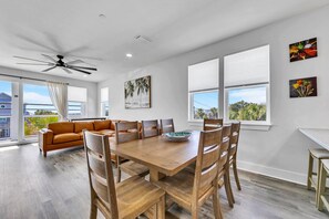 Un'ampia zona pranzo con tavolo e sedie in legno, una ventola a soffitto e ampie finestre con vista sull'esterno.