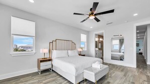 A modern bedroom with a large bed, bedside tables, a ceiling fan, and a view through a window.