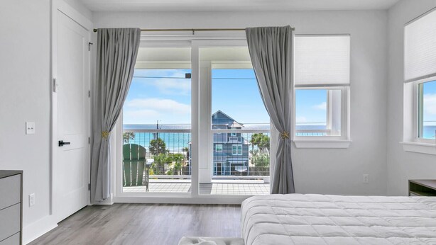 A bedroom with a large bed, a balcony with a view of the sea, and a sliding glass door.