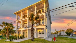 A multi-story residential building with a balcony on the second floor, a well-maintained lawn, and a palm tree in the foreground.