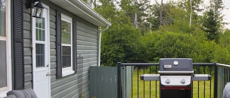 A patio with a grill, wicker furniture, and a house with shutters.