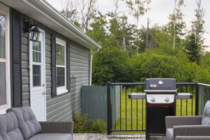 A patio with a grill, wicker furniture, and a house with shutters.