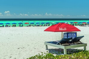 Una playa con sillas de descanso y sombrillas, un cartel que anuncia cerveza bien fría, y el océano al fondo.