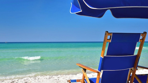 A beach chair and umbrella on a sandy beach with clear turquoise water and a clear sky.