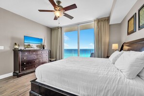 Habitación de hotel con una cama grande, ventilador de techo, cómoda, televisor y vistas al océano.