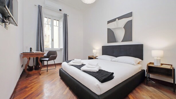 Una habitación de hotel moderna con una cama grande, un escritorio, una silla y una ventana con cortinas.