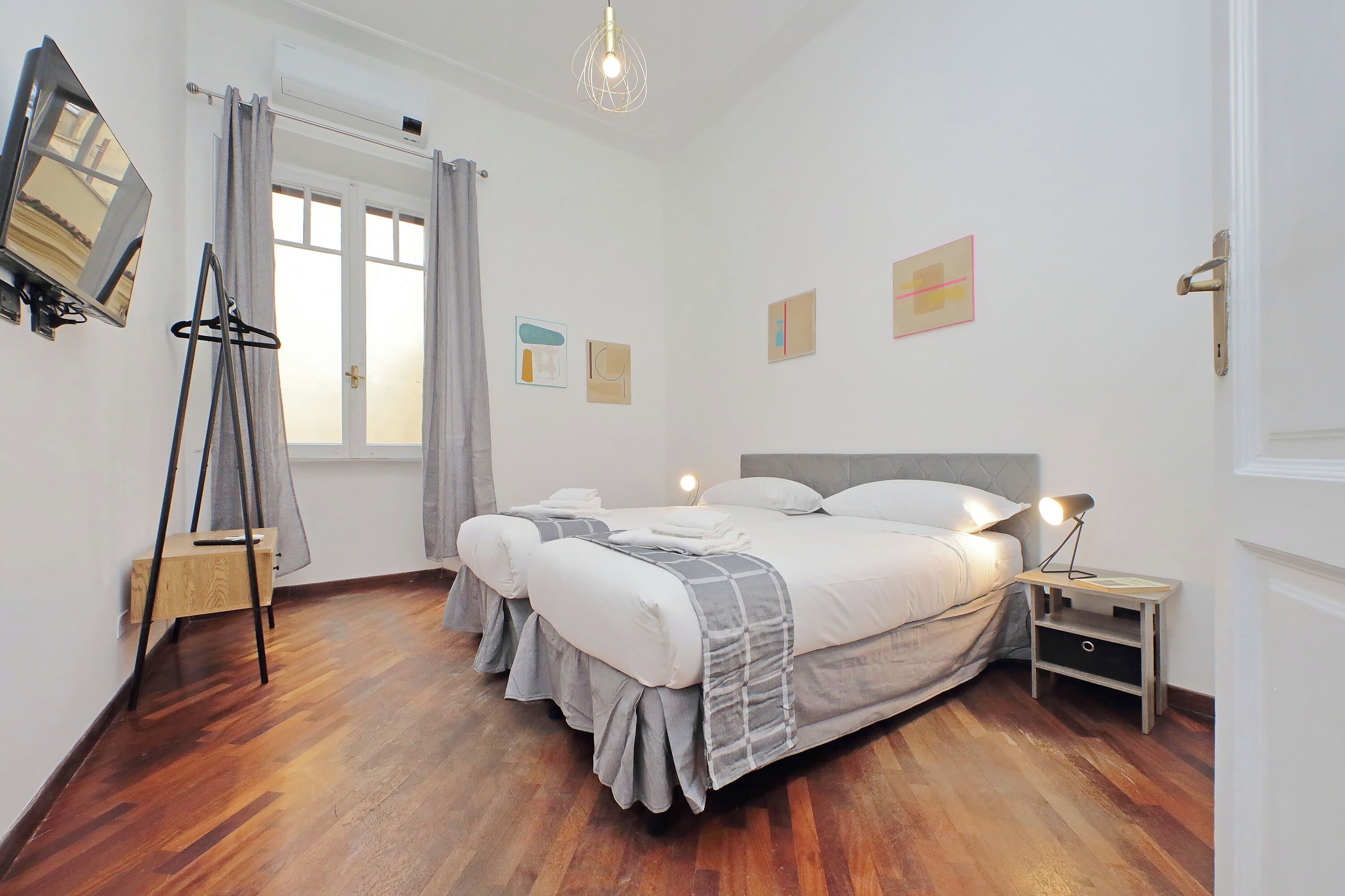 A bedroom with a double bed, a bedside table with a lamp, a TV on the wall, and artwork on the wall.