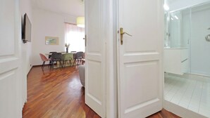 Una habitación con piso de madera, un comedor con sillas y una mesa, y un área de ducha con puerta de vidrio.