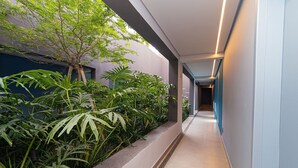 A modern hallway with a concrete planter filled with tropical plants, a tiled floor, and a light-colored wall. - Vossa Bossa Pop Pinheiros (São Paulo)