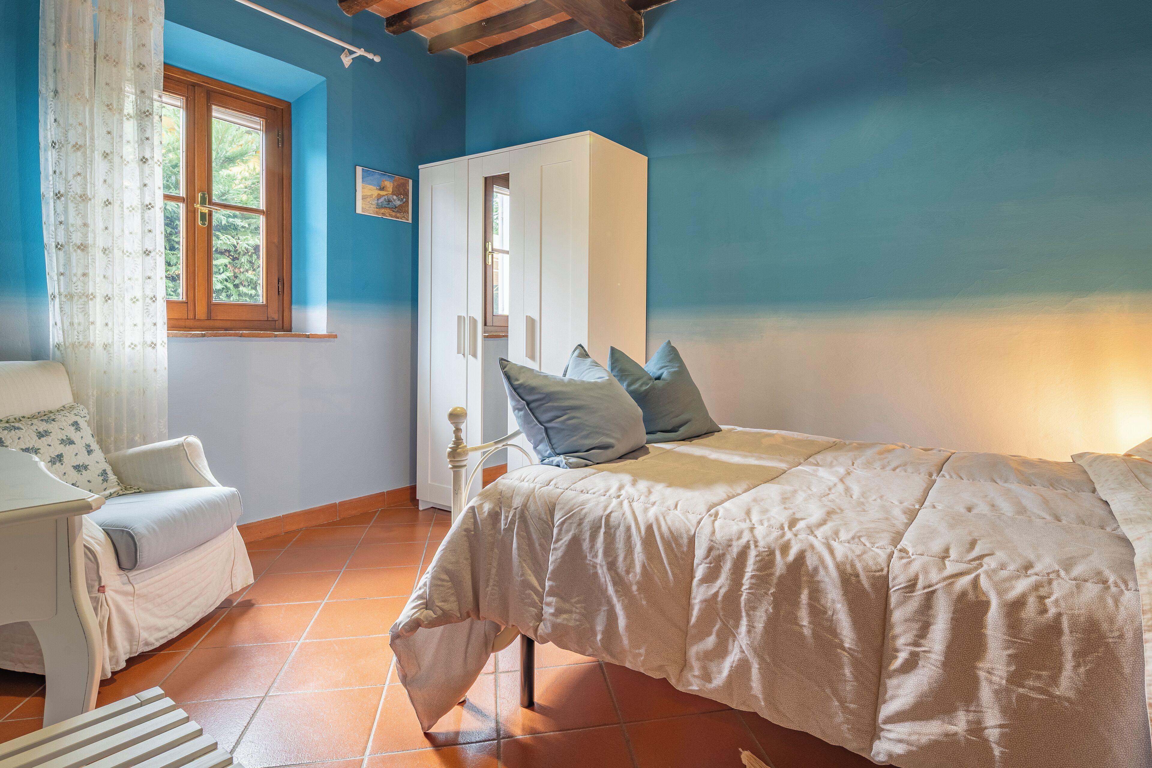 Een slaapkamer met een bed, een stoel, een garderobe en een raam met gordijnen.