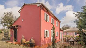 Stunning two-story building with a red facade and white shutters, set amidst a tranquil garden with a pergola and seating area.