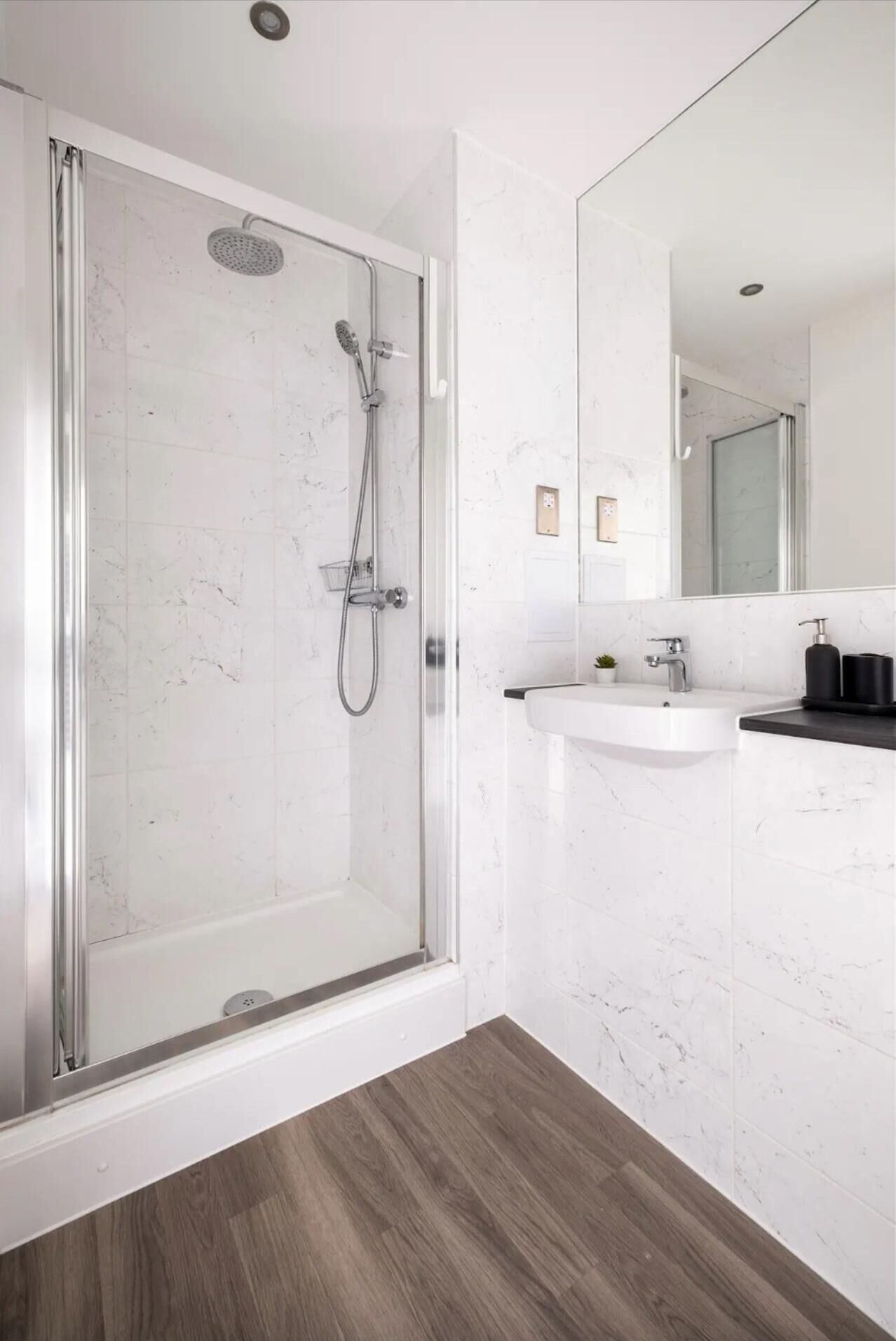 A modern bathroom with a glass-enclosed shower, a white sink, and a large mirror.