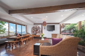 A spacious living area with a wooden bench seating, a wicker sofa, and a large window offering a view of the outdoors.