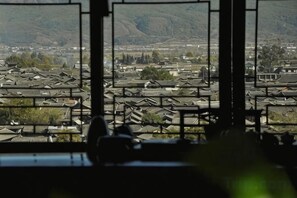 A view through a window with a grid pattern, overlooking a residential area with multiple buildings and a hilly landscape in the distance. - Mulan Villa (Lijiang)