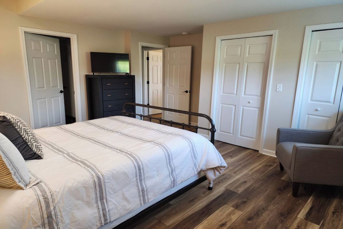 Quarto com cama, cômoda, televisão e duas portas.
