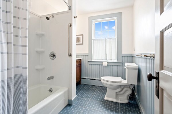 Une salle de bain avec une baignoire, une douche, des toilettes et une fenêtre.