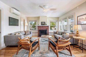 A spacious living room with two sofas, a fireplace, a ceiling fan, and large windows.