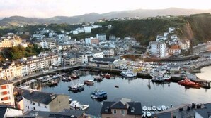 Un pueblo costero con un puerto deportivo lleno de barcos, edificios a lo largo de la costa y colinas al fondo.