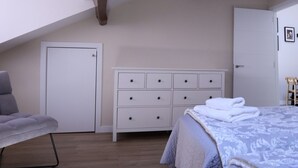 Un dormitorio con una cama, un aparador, un sillón gris y una puerta.