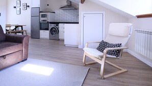 Una sala de estar moderna con un sofá, una butaca con un cojín estampado y una cocina al fondo.