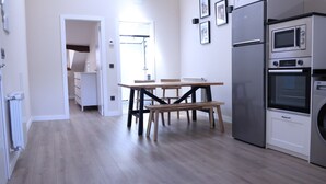 Una cocina moderna con horno integrado, microondas y lavadora, una mesa de madera con bancos, y vistas al área de estar contigua.