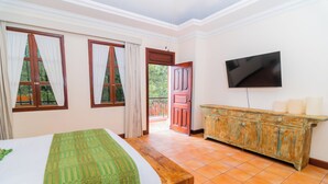 A bedroom with a bed, a wooden bench, a TV, and a door leading outside.