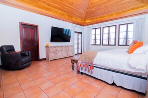 A bedroom with a bed, a TV, a wooden ceiling, and a window.