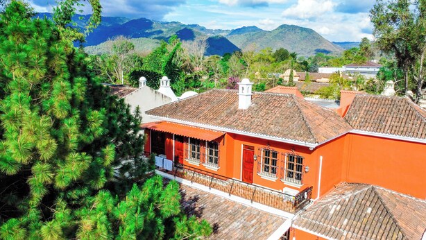 A traditional building with a tiled roof, surrounded by lush greenery and mountains in the background.