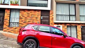 Un auto rojo estacionado frente a un edificio moderno con múltiples ventanas y fachada de ladrillo.