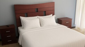 Una cama bien hecha con cabecera de madera, dos mesitas de noche y un velador.
