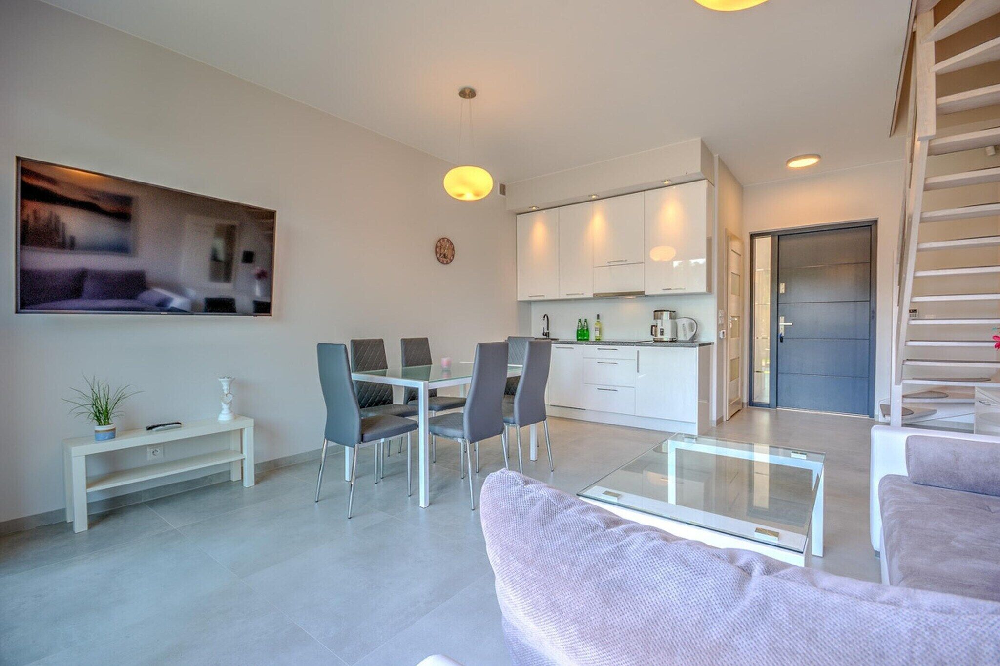 Een moderne woonkamer met een glazen salontafel, grijze banken en een eethoek met stoelen en een tafel.