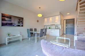 A modern living room with a glass coffee table, grey sofas, and a dining area with chairs and a table. - Comfortable holiday home with a garden and a pool (Pobierowo)