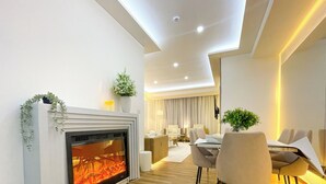 Un salon moderne doté d’une cheminée, d’un coin repas avec une table et des chaises, et d’un espace détente avec un canapé et des lampes.