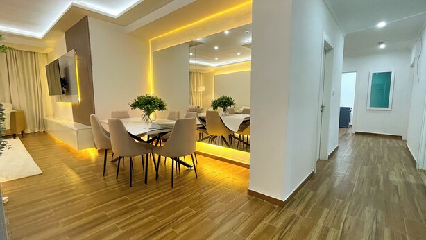Un salon moderne comprenant un coin repas, un parquet en bois et un grand miroir qui agrandit visuellement l’espace.