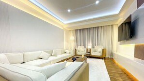 Un salon moderne avec un canapé d’angle, deux fauteuils, une table basse et un téléviseur à écran plat fixé au mur.