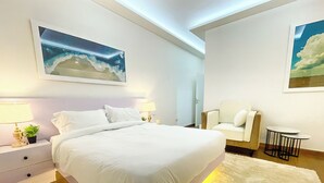 Une chambre moderne avec un grand lit, des tables de chevet, une chaise, une petite table ronde et deux tableaux accrochés au mur.