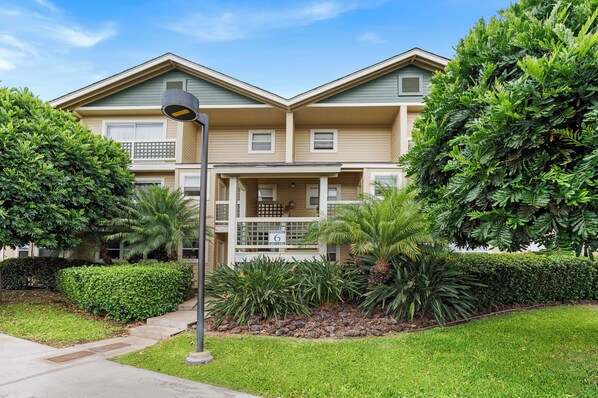 A two-story residential building with a balcony, surrounded by well-maintained landscaping and a clear sky. - Summer Deal Waikoloa Hills 2BR Condo with Pool Hot Tub and Views (Waikoloa)