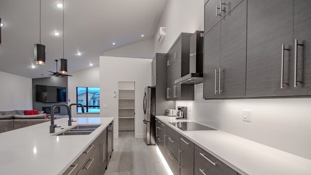 A modern kitchen with a central island, stainless steel appliances, and a view to the living area. - Crimson Place - Moab Home with a Private Pool! (Moab)