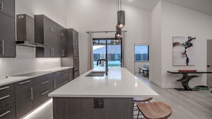 A modern kitchen with dark cabinets, a white island, and pendant lighting. - Crimson Place - Moab Home with a Private Pool! (Moab)