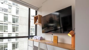 A modern office space with a large window, a desk with a chair, a television, and a shelf with items. - Nuo by Wynwood House  (Bogotá)