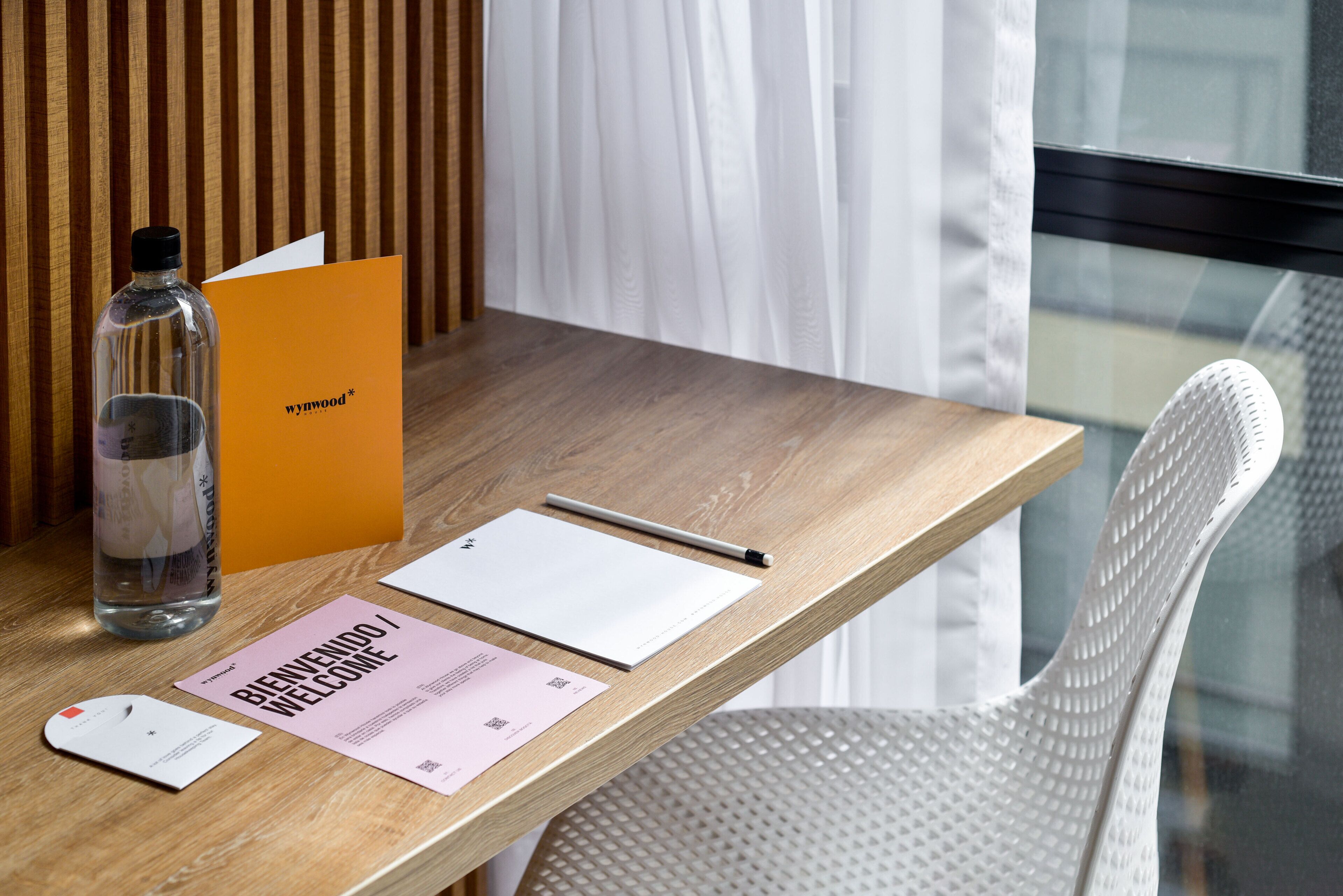 A wooden desk with a bottle, a pen, a notepad, and a welcome card.
