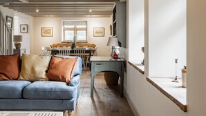 A cozy living room with a blue sofa, wooden dining table, and a staircase leading to an upper floor. - A Pretty Norfolk Cottage (Field Dalling)