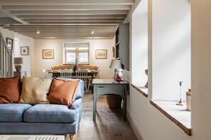 A cozy living room with a blue sofa, wooden dining table, and a staircase leading to an upper floor.
