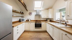 A modern kitchen with white cabinetry, a wooden countertop, a built-in oven, a microwave, and a skylight. - A Pretty Norfolk Cottage (Field Dalling)