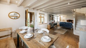 A dining area with a wooden table set for four, a blue sofa, and a fireplace in the background. - A Pretty Norfolk Cottage (Field Dalling)