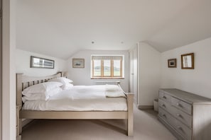 A bedroom with a bed, a dresser, a radiator, and a window with a view of greenery.